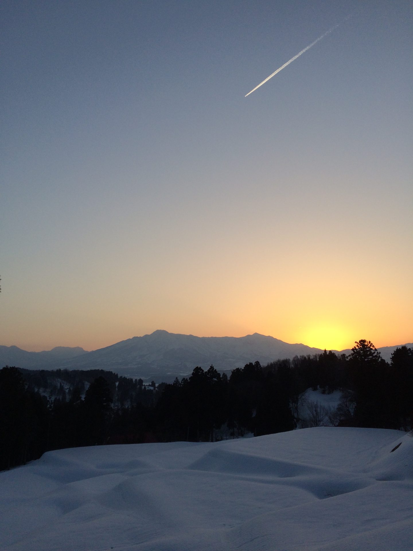 雪の積もった里山に沈む夕日